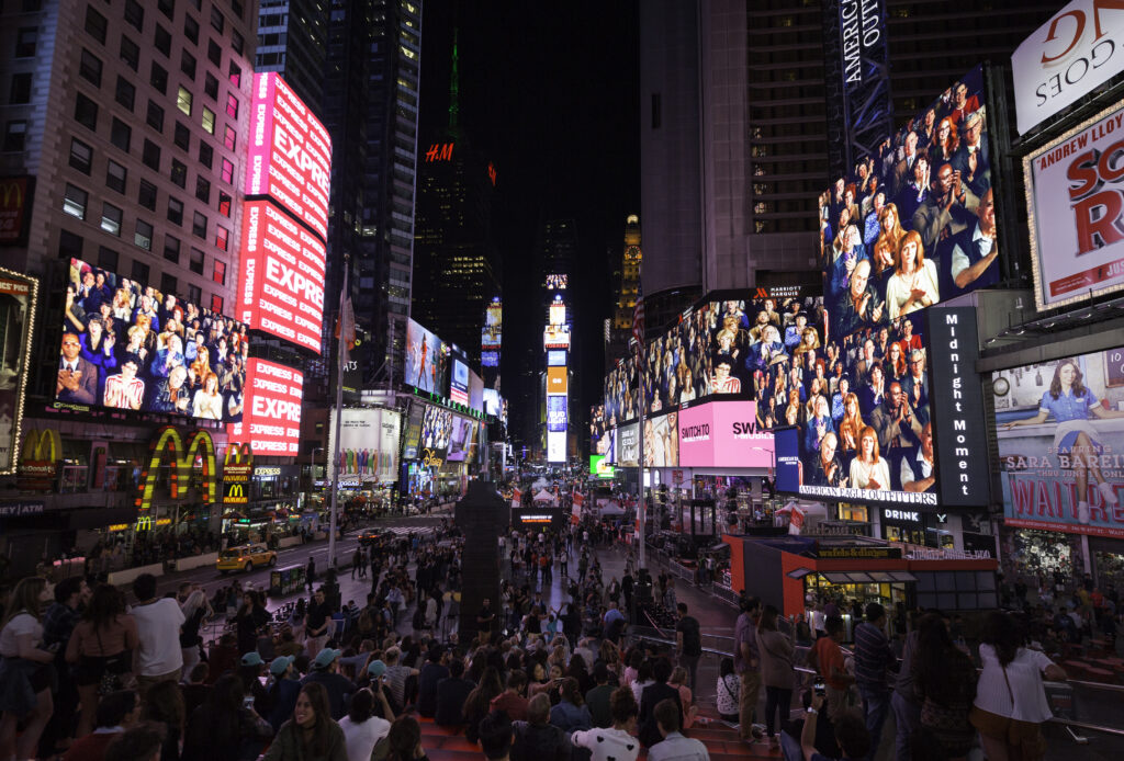 Alex Prager's digital artwork, Applause, is displayed on electronic billboards in Times Square, showing people in theatre auditorium clapping for the pedestrians below the screens in the plazas.
